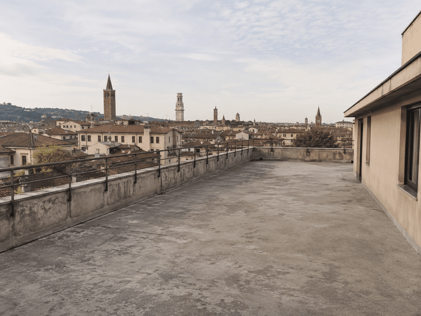 Attico nel centro storico di Verona prima: terrazzo vuoto in cemento con vista sulle torri della città